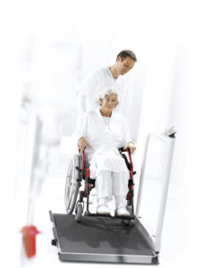 1289990937c seca 677 676 patient in wheelchair on scale rgb600h 227x300 - SECA 677 Elektroniczna waga do wózków inwalidzkich